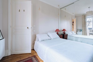 Een slaapkamer met een bed, nachtkastje met lamp, een dressoir en een grote spiegel.