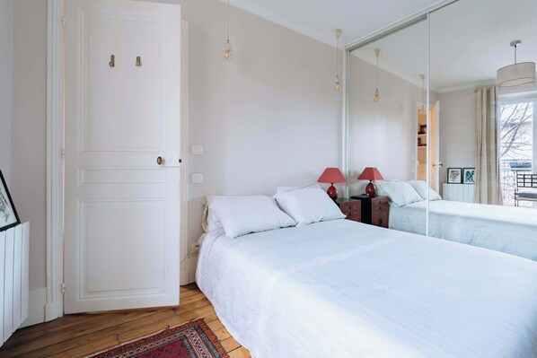 A bedroom with a bed, a nightstand with a lamp, a dresser, and a large mirror.