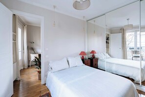 A bedroom with a large mirror, a bed, bedside tables, and a view of the outside.
