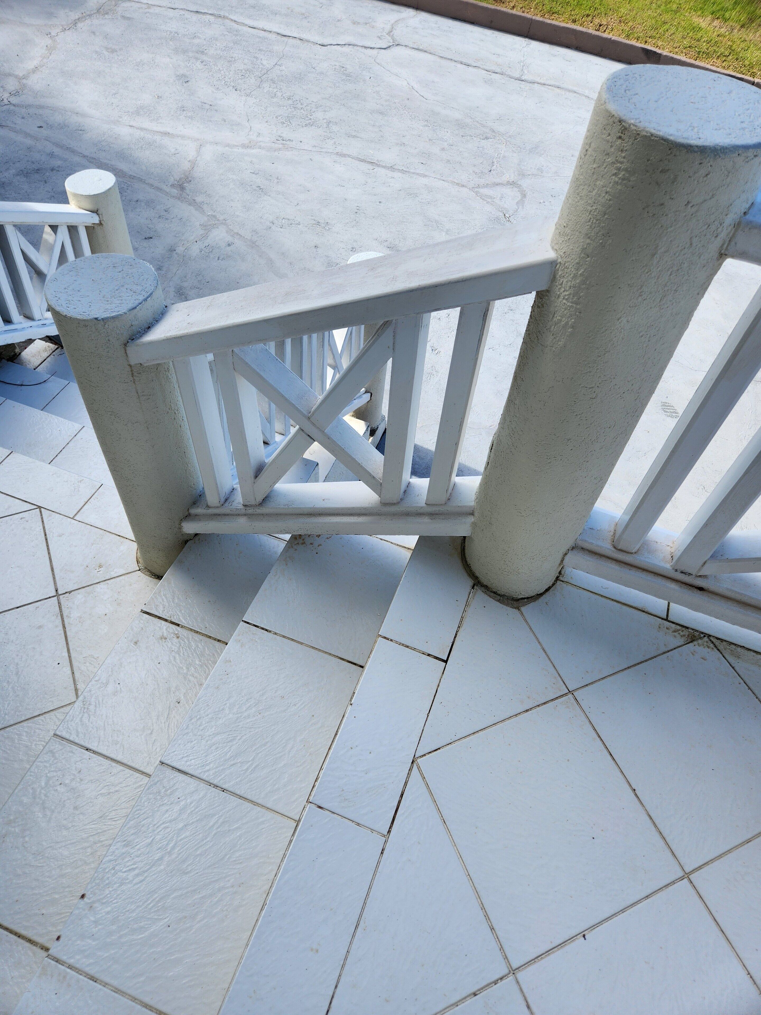 Une porte en métal blanc, ornée d’une barre transversale, est installée sur une terrasse carrelée.