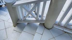 A white metal gate with a crossbar design, set on a tiled patio area. - Sunset Nook: Cozy one bedroom apartment

 (Saint James)