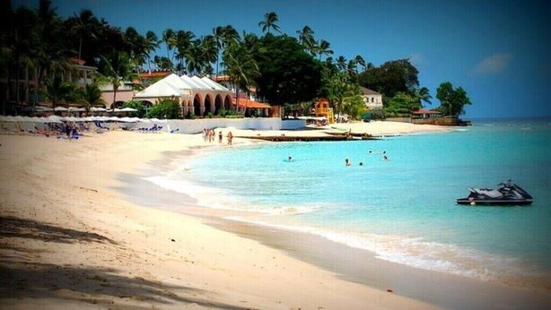 A beach with a clear blue sea, a sandy shore, and a few people swimming. There are palm trees and buildings in the background. - Sunset Nook: Cozy one bedroom apartment

 (Saint James)