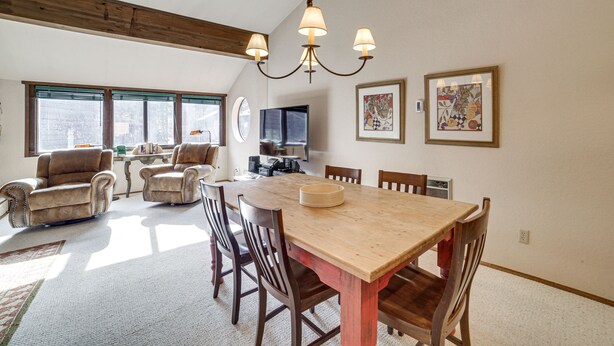 A spacious living room with a wooden dining table, multiple chairs, a fireplace, and a large window. - Mammoth Lakes Condo: Walk to Village & Gondola! (Mammoth Lakes)