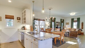 Un'ampia cucina con isola centrale, zona pranzo con sedie e tavolo, e un soggiorno con divano e tavolino.