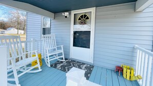 A porch with a white rocking chair, a yellow chair, and a white bench.