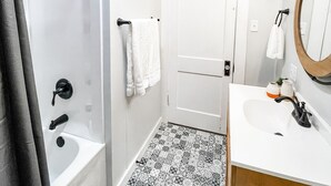 A bathroom with a shower, a sink, a mirror, and patterned floor tiles.