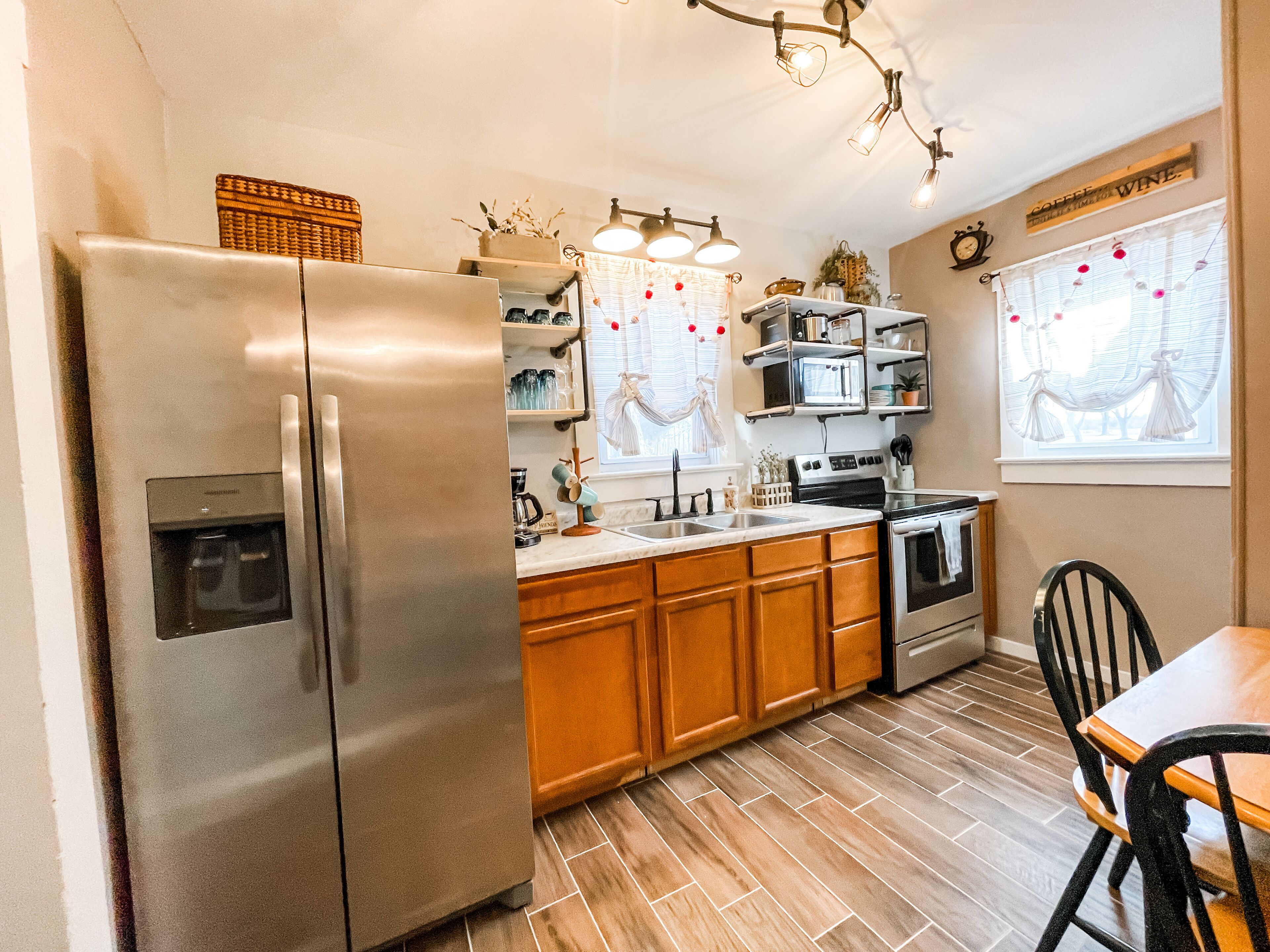A kitchen with a stainless steel refrigerator, wooden cabinets, a built-in oven, and a dining area with a table and chairs.