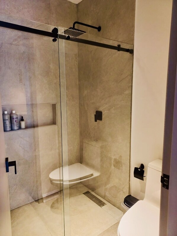 A modern bathroom with a glass-enclosed shower, a toilet, and a shelf with toiletries. - Espectacular casa en la Zona Rosa Cali (Cali)