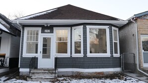 Une maison à deux étages, avec une façade de couleur gris foncé, des éléments décoratifs blancs et le numéro « 242 » sur la porte d’entrée.