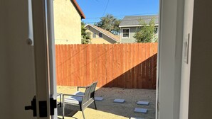 On aperçoit, à travers une porte, un jardin avec une clôture en bois, une table de patio et une chaise.