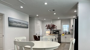 Une cuisine moderne avec des meubles blancs, un coin repas avec des chaises blanches et un tableau accroché au mur.