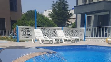 A swimming pool with a water feature, a beach ball, and lounge chairs.