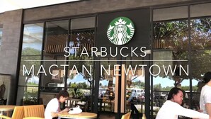 Fachada de un Starbucks en Magtan Newtown con amplios ventanales y mesas al aire libre.