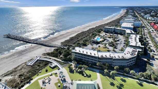 Vista aérea de un hotel frente al mar, con un paseo marítimo, un muelle y un estacionamiento.