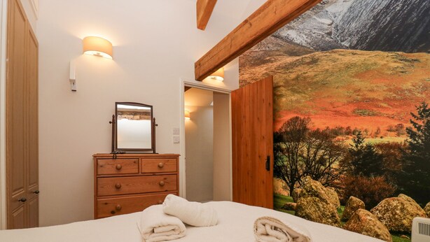 A bedroom with a bed, wooden dresser, and a mural of a landscape. - Taylor's Cottage (Keswick)