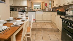 A kitchen with white cabinets, a wooden dining table, and a black stove. - Taylor's Cottage (Keswick)
