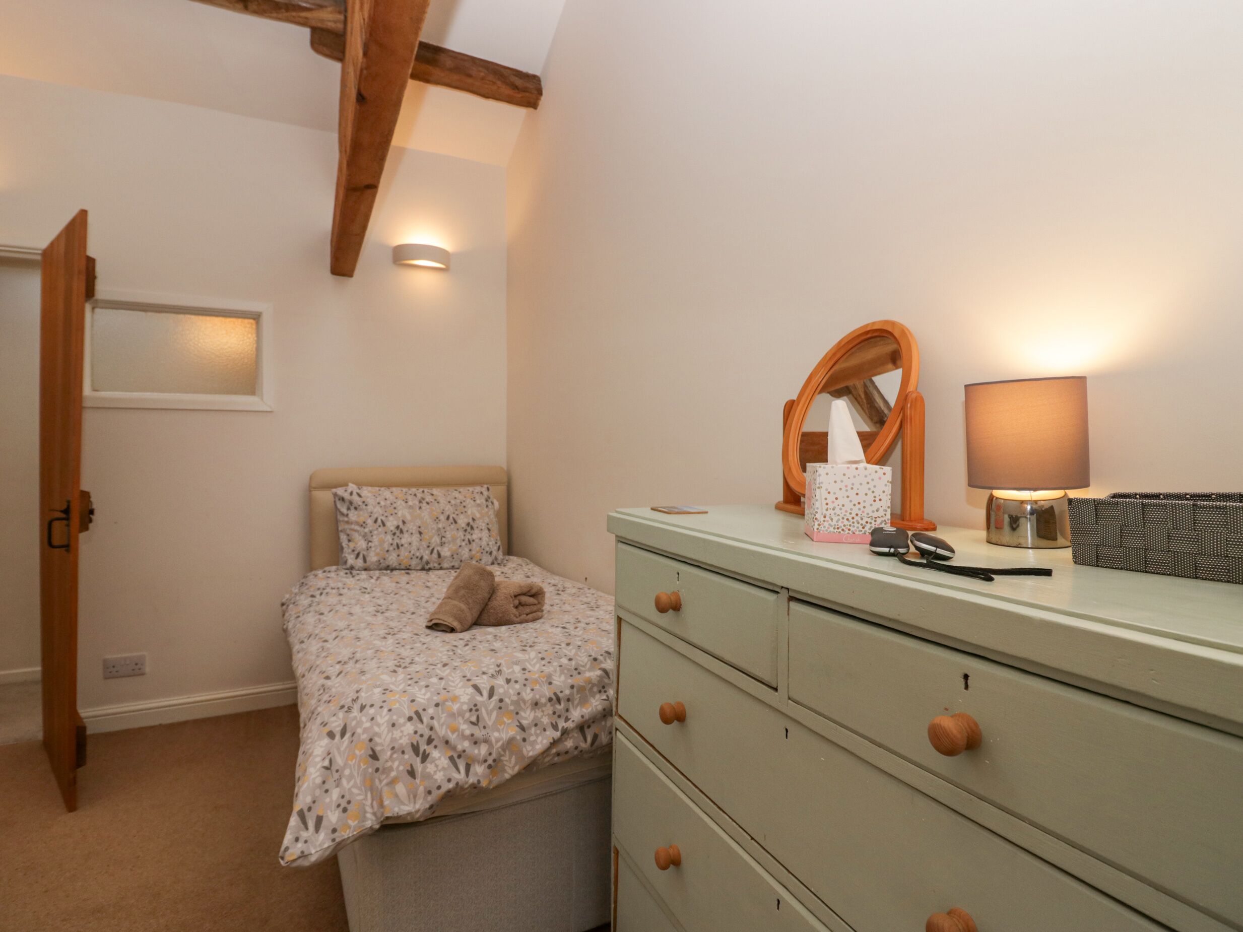 A bedroom with a bed, a dresser, a mirror, a lamp, and a bedside table.