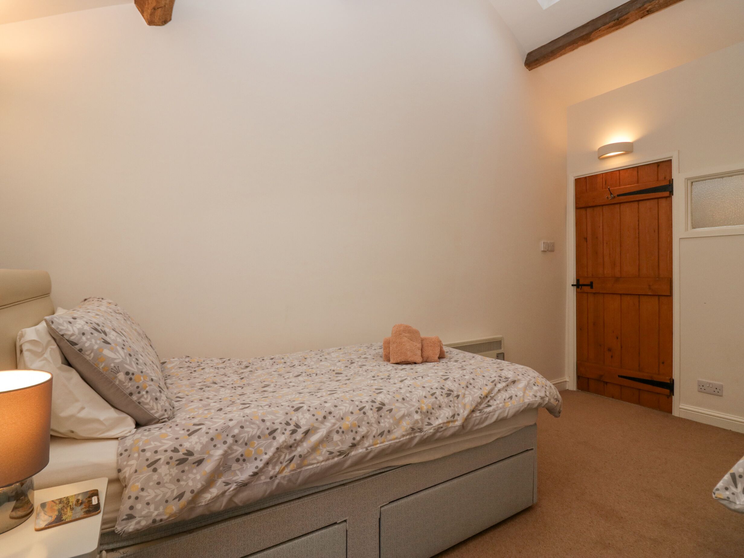 A bedroom with a bed, a nightstand, a lamp, a teddy bear, and a wooden door.