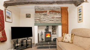 A cozy living room with a stone fireplace, a television, and a sofa. - Taylor's Cottage (Keswick)