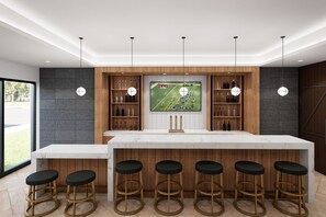 Une cuisine moderne dotée d’un grand îlot central, de tabourets de bar et d’un téléviseur fixé au-dessus de l’îlot, diffusant un événement sportif.