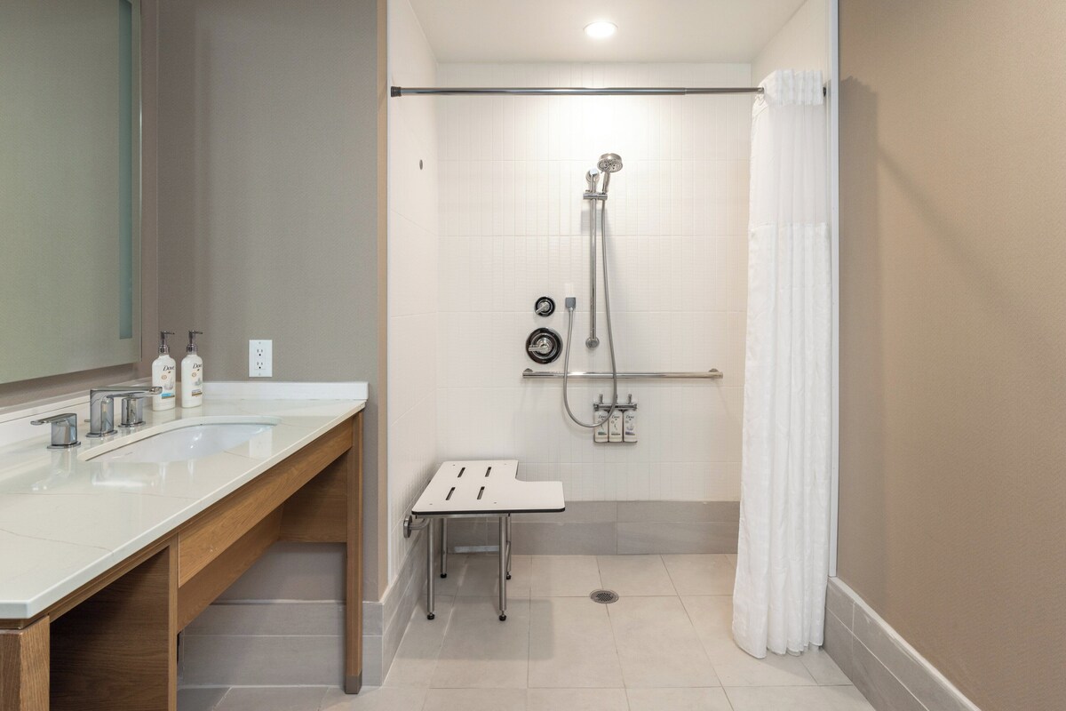 Un baño moderno con dos lavamanos, ducha y una pequeña mesa.