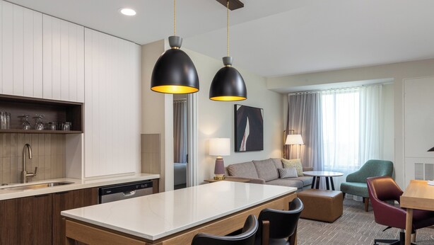 Una habitación de hotel moderna con cocina, una mesa de comedor con sillas, un sofá y una lámpara.