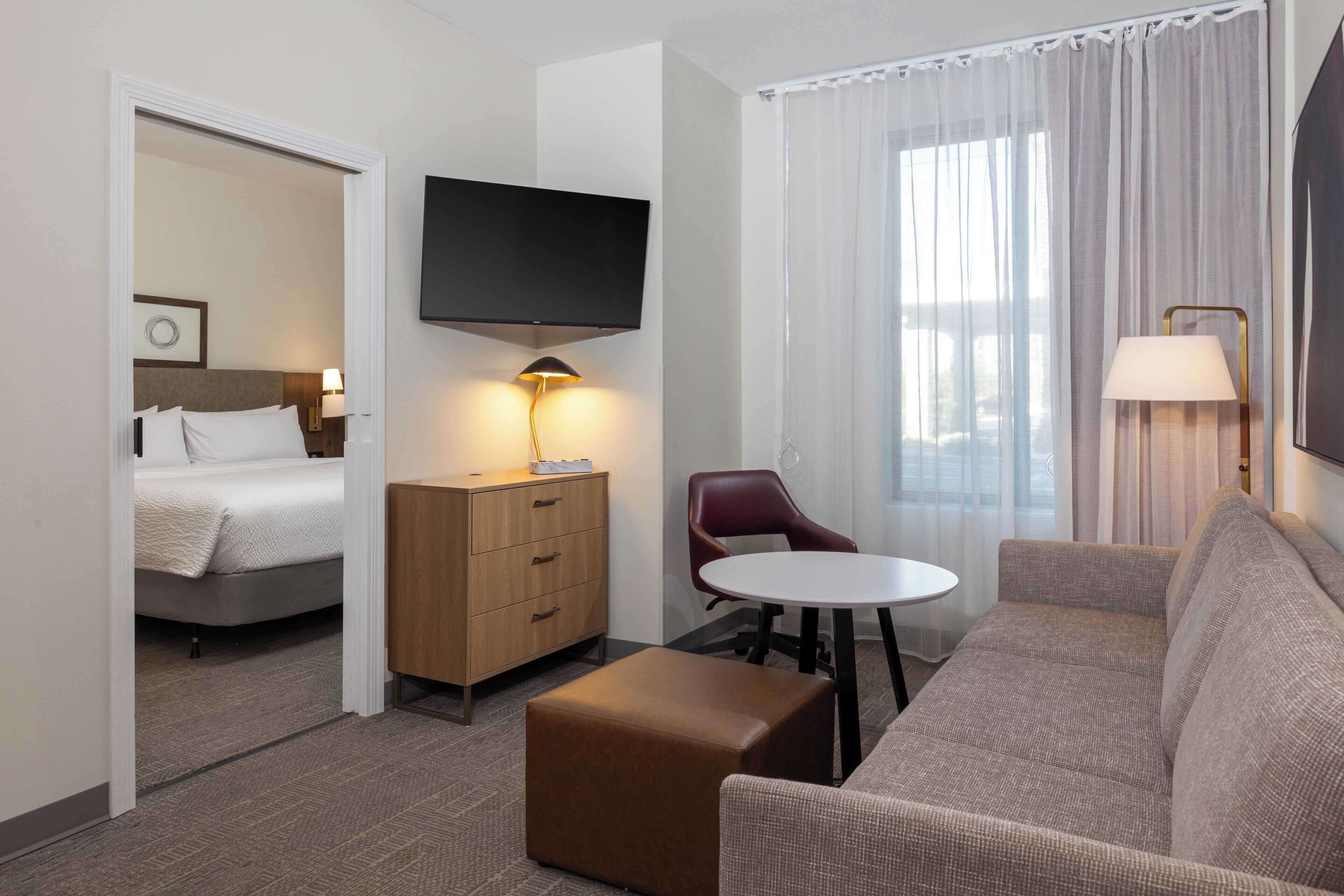 A hotel room with a bed, a TV, a desk with a lamp, a sofa, and a view of the outdoors.
