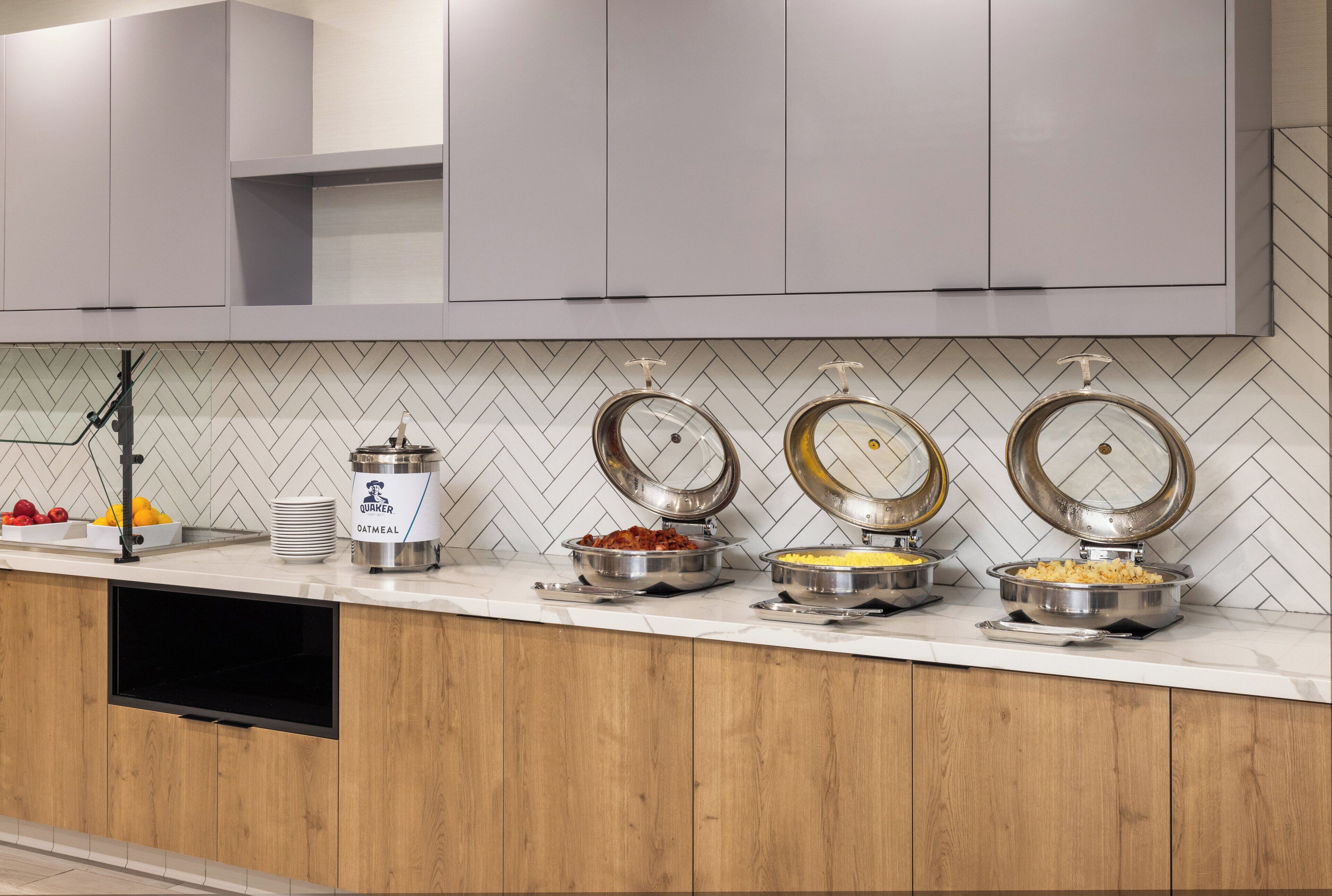 A modern kitchen with a herringbone tile backsplash, a built-in oven, and a variety of food containers on the counter.