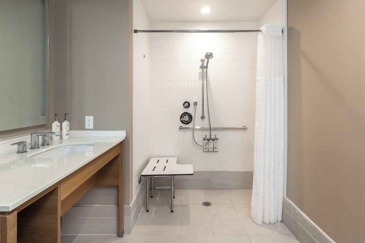 Un baño moderno con dos lavamanos, ducha y una pequeña mesa.