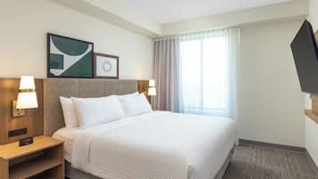 Una habitación de hotel con una cama grande, dos mesitas de noche con lámparas, un televisor montado en la pared y una ventana con cortinas.