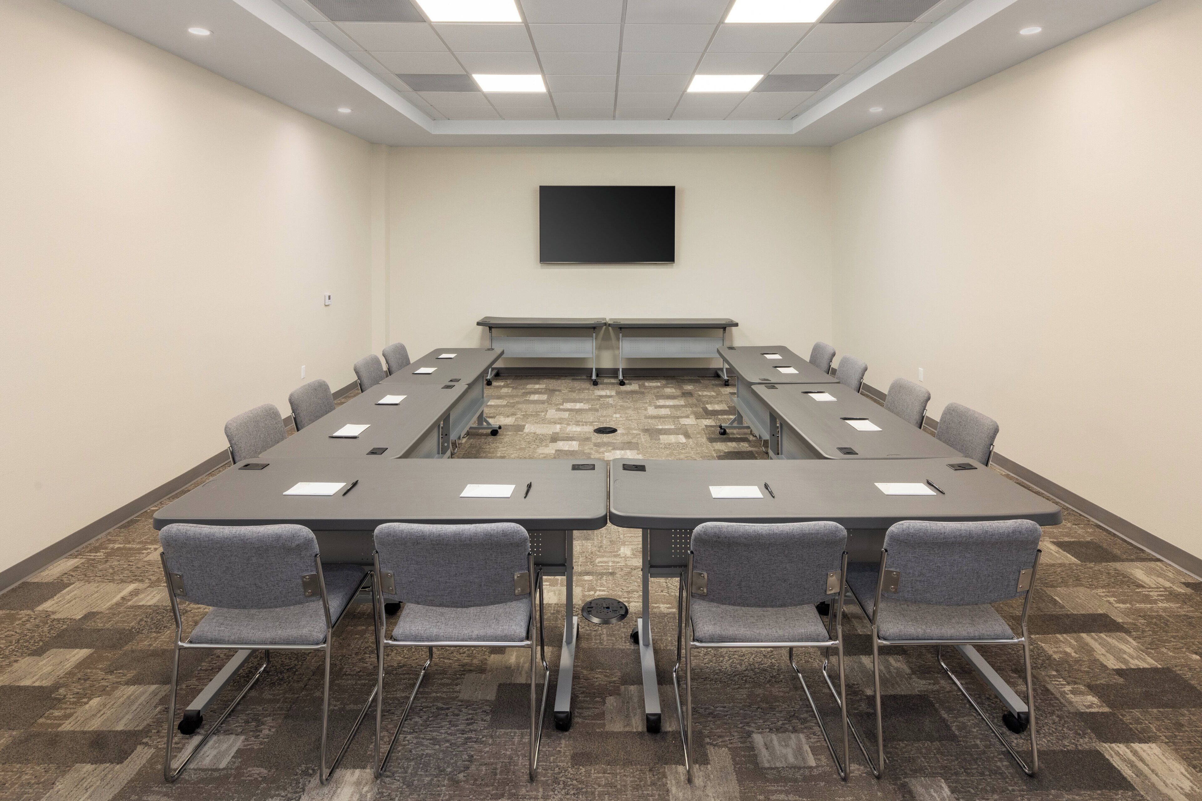 Une salle de conférence dotée d’une longue table, de nombreuses chaises, d’un téléviseur à écran plat et d’un revêtement de sol en moquette.