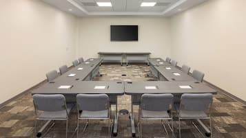 Une salle de conférence dotée d’une longue table, de nombreuses chaises, d’un téléviseur à écran plat et d’un revêtement de sol en moquette.
