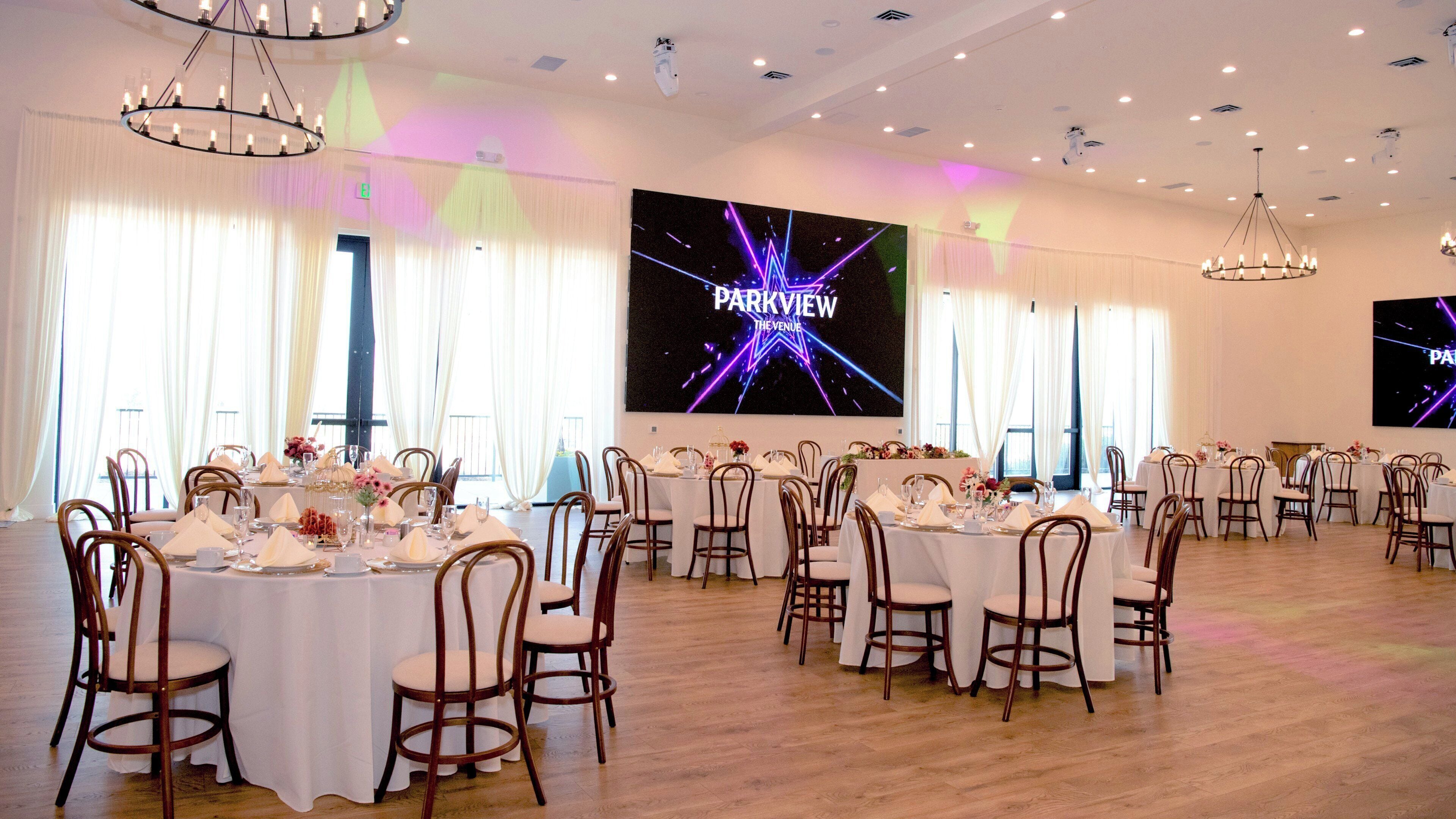A banquet hall with round tables set for dining, wooden chairs, and chandeliers.