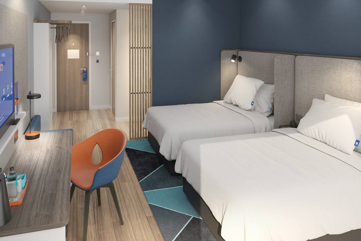 A hotel room with two beds, a desk, a chair, and a TV.