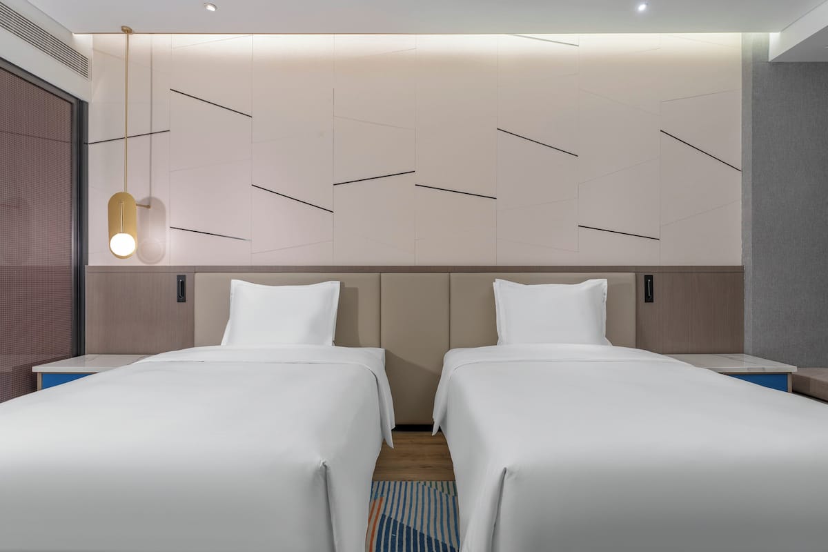 A hotel room with two beds, a modern light fixture, and a patterned wall.