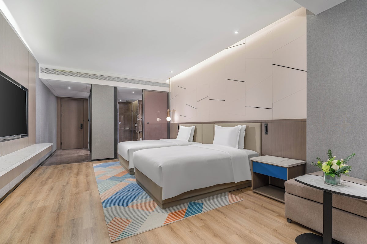 A modern hotel room with two beds, a desk, and a TV.