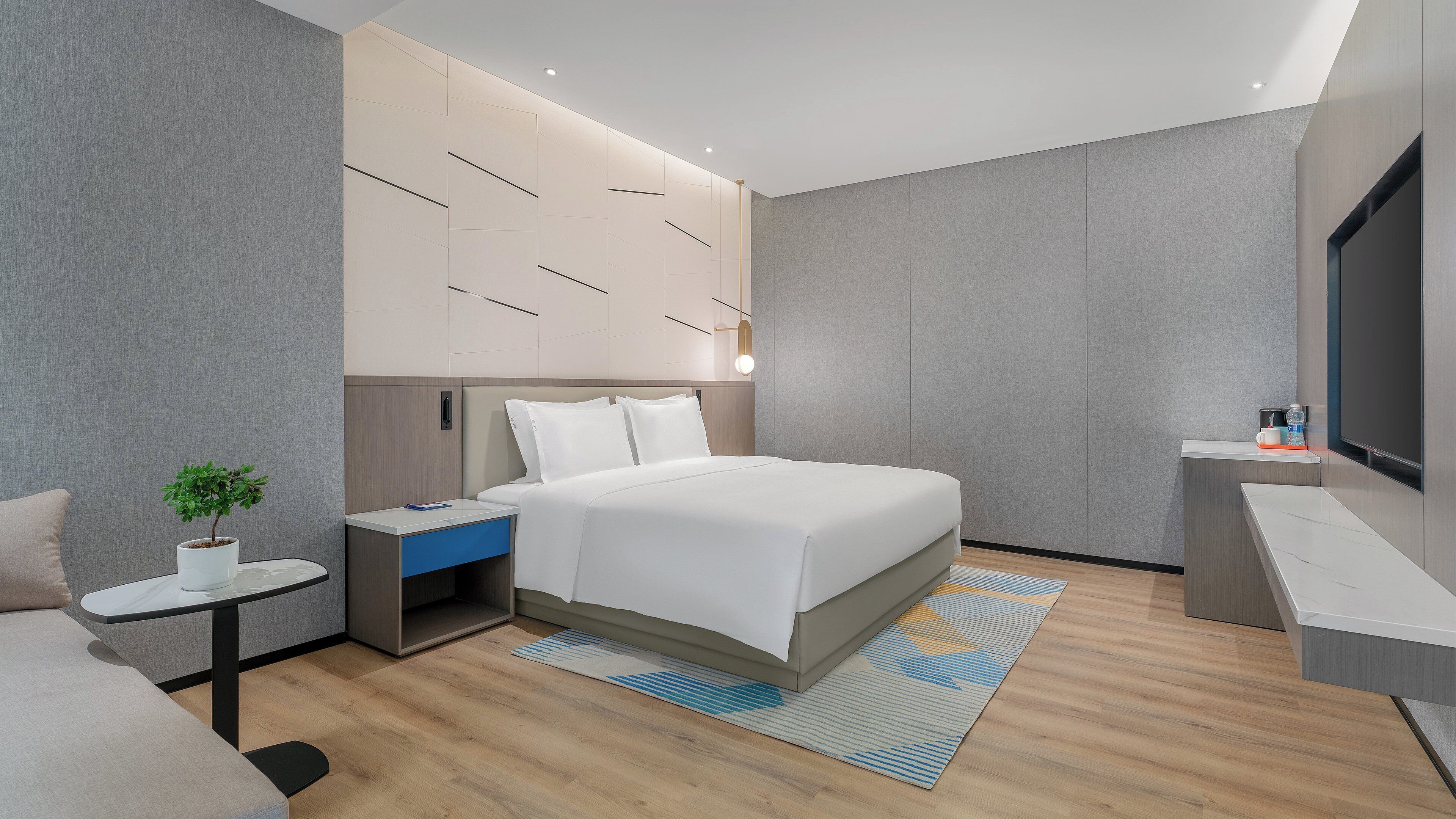 A modern hotel room with a bed, bedside table, nightstand, and a small desk with a TV.