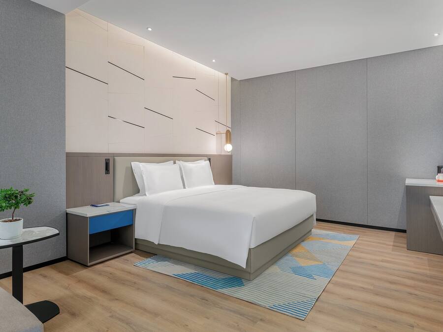 Ein modernes Hotelzimmer mit Bett, Nachttisch, einer kleinen Schreibtisch und Fernseher.