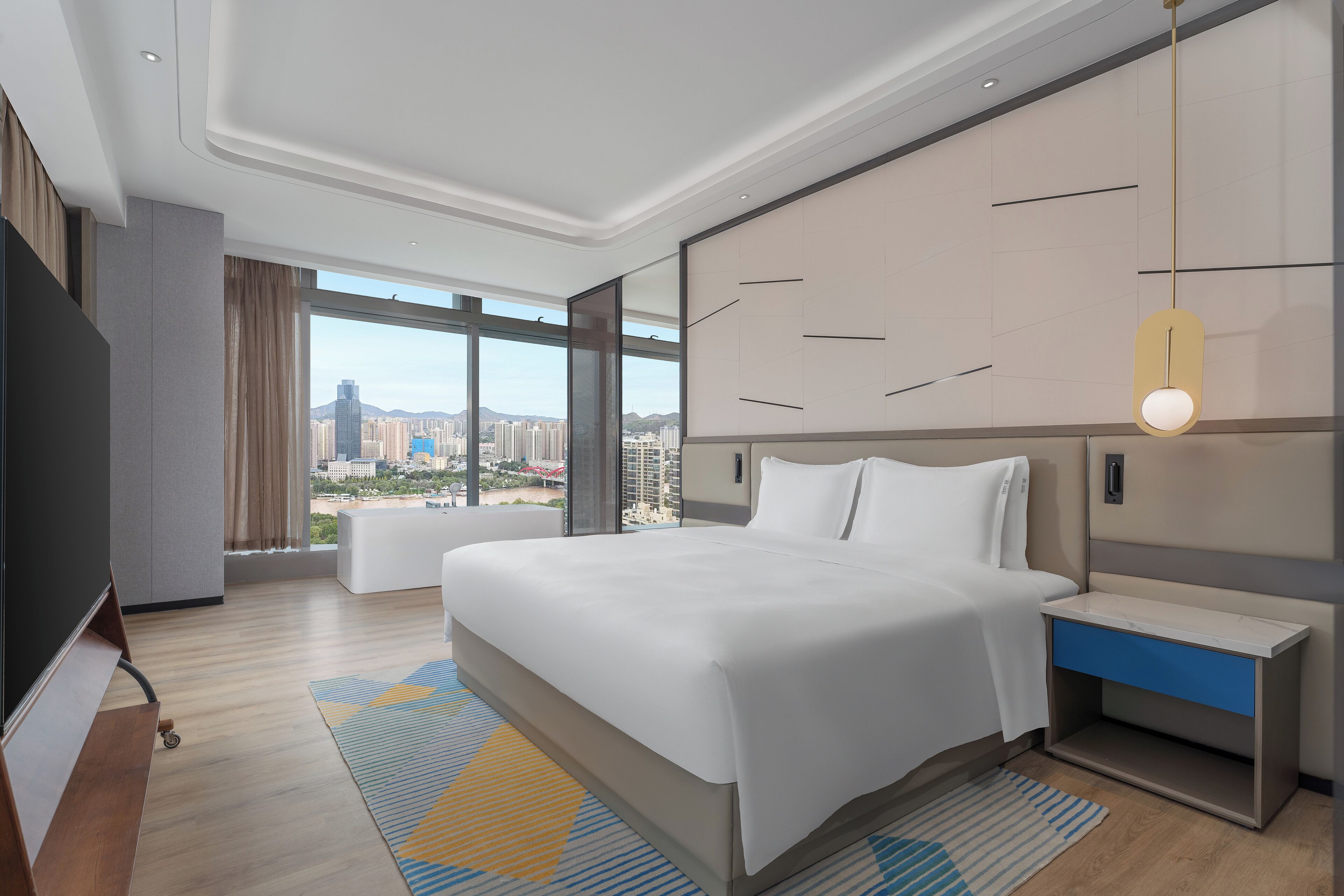A modern hotel room with a large bed, a bedside table with a drawer, a TV, and a large window offering a city view.