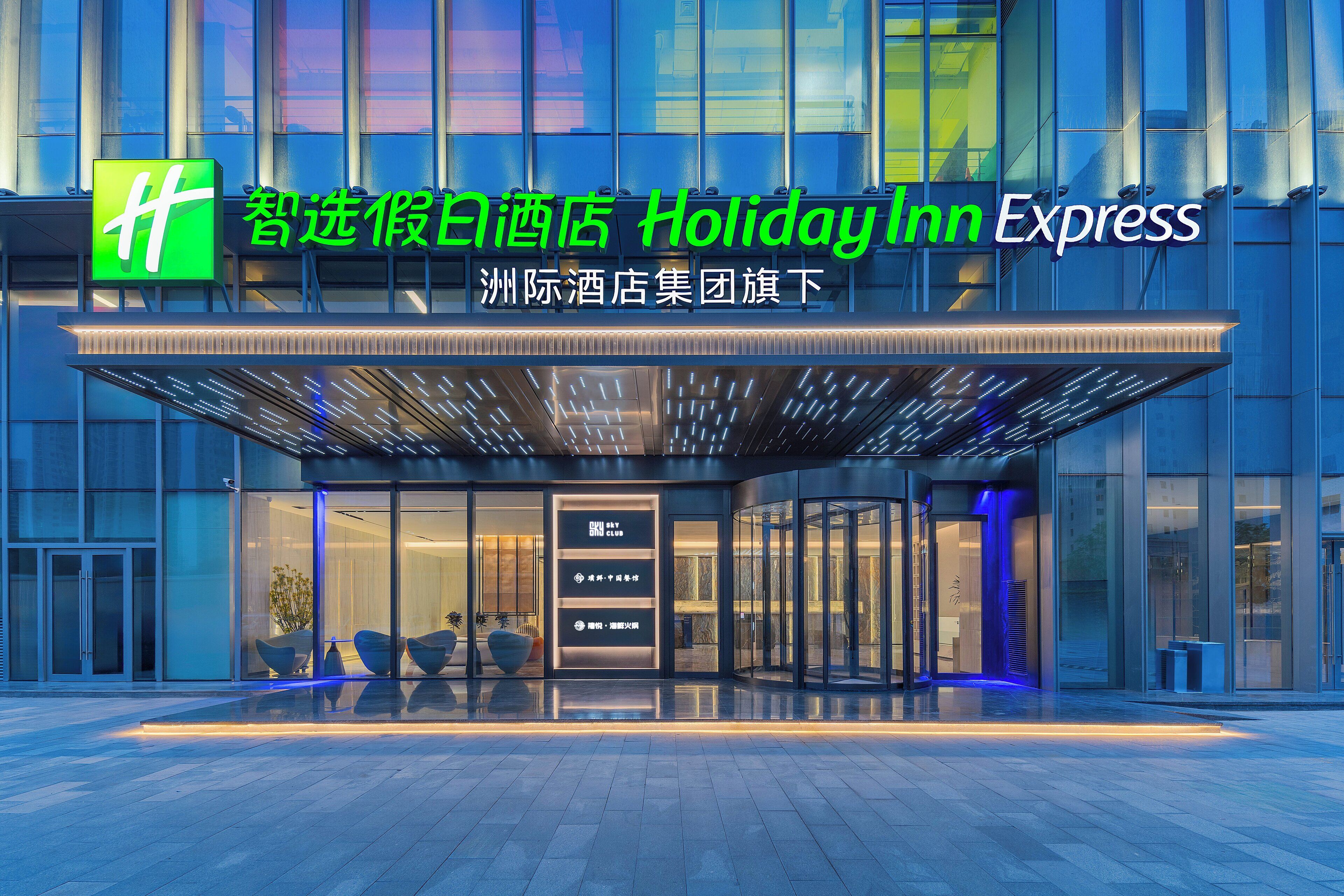 Entrada de un hotel Holiday Inn Express con diseño moderno, puertas de vidrio y fachada bien iluminada.