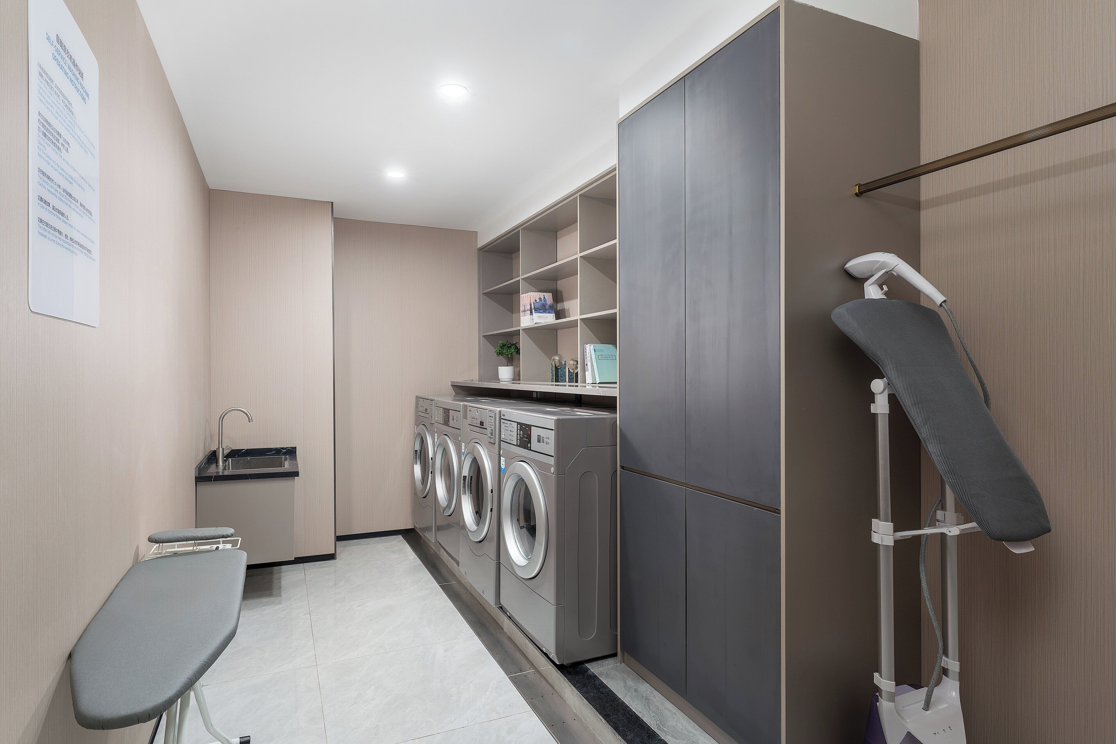 A laundry area with a washing machine, dryer, ironing board, and a towel rack.