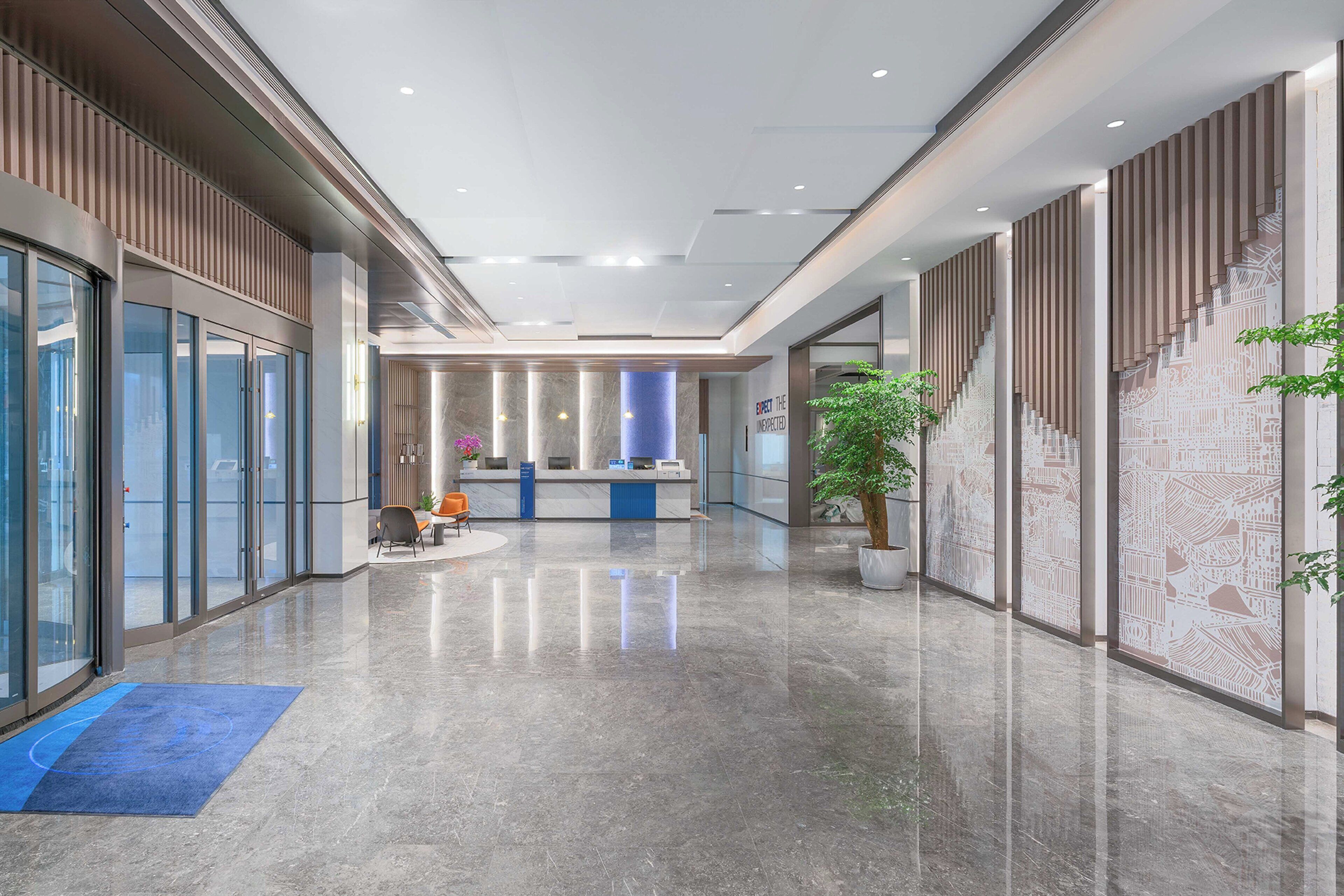 Un moderno vestíbulo de hotel con mostrador de recepción, puertas de cristal y una alfombra azul.