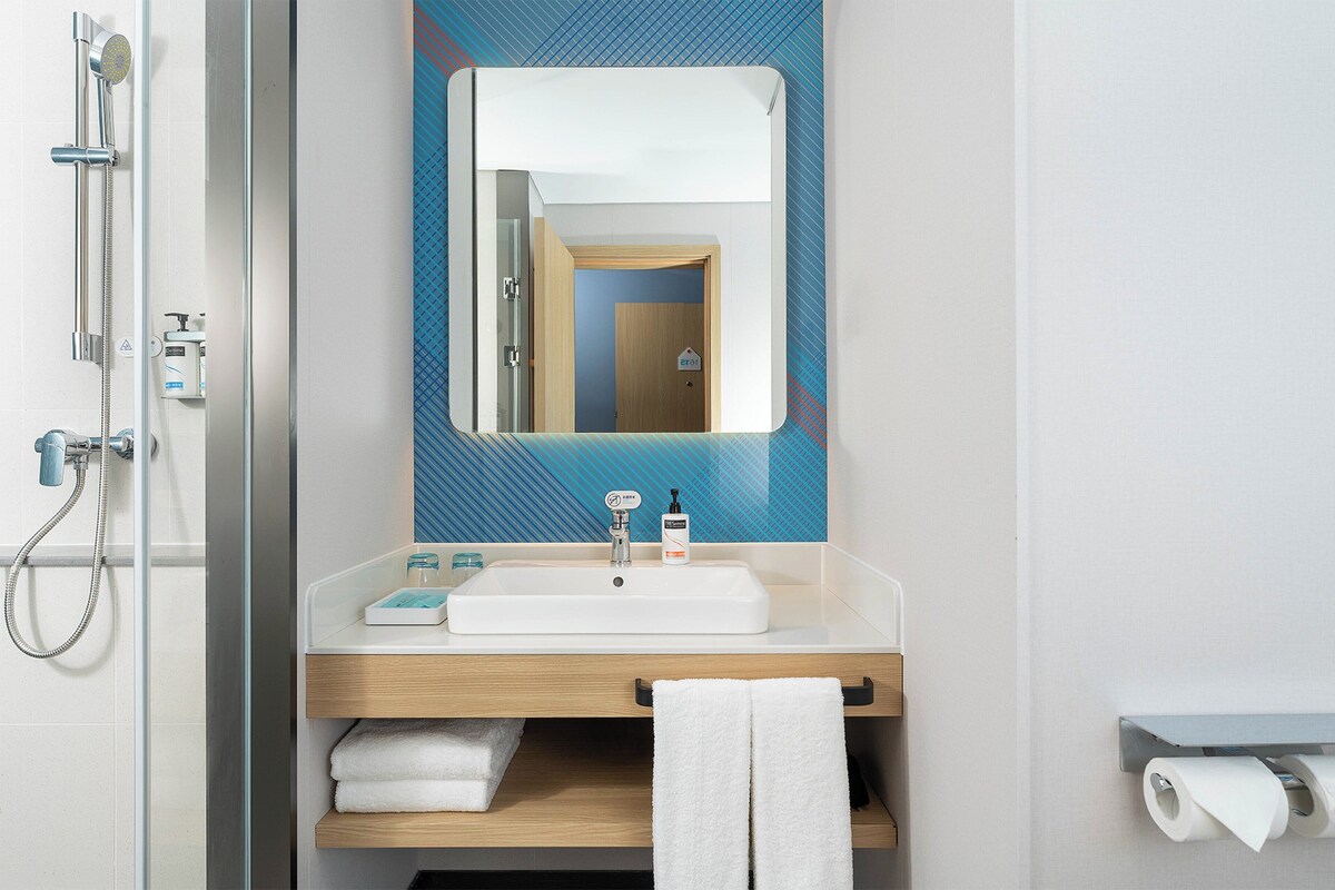 A modern bathroom with a glass-enclosed shower, a white sink with a soap dispenser, and a towel rack.