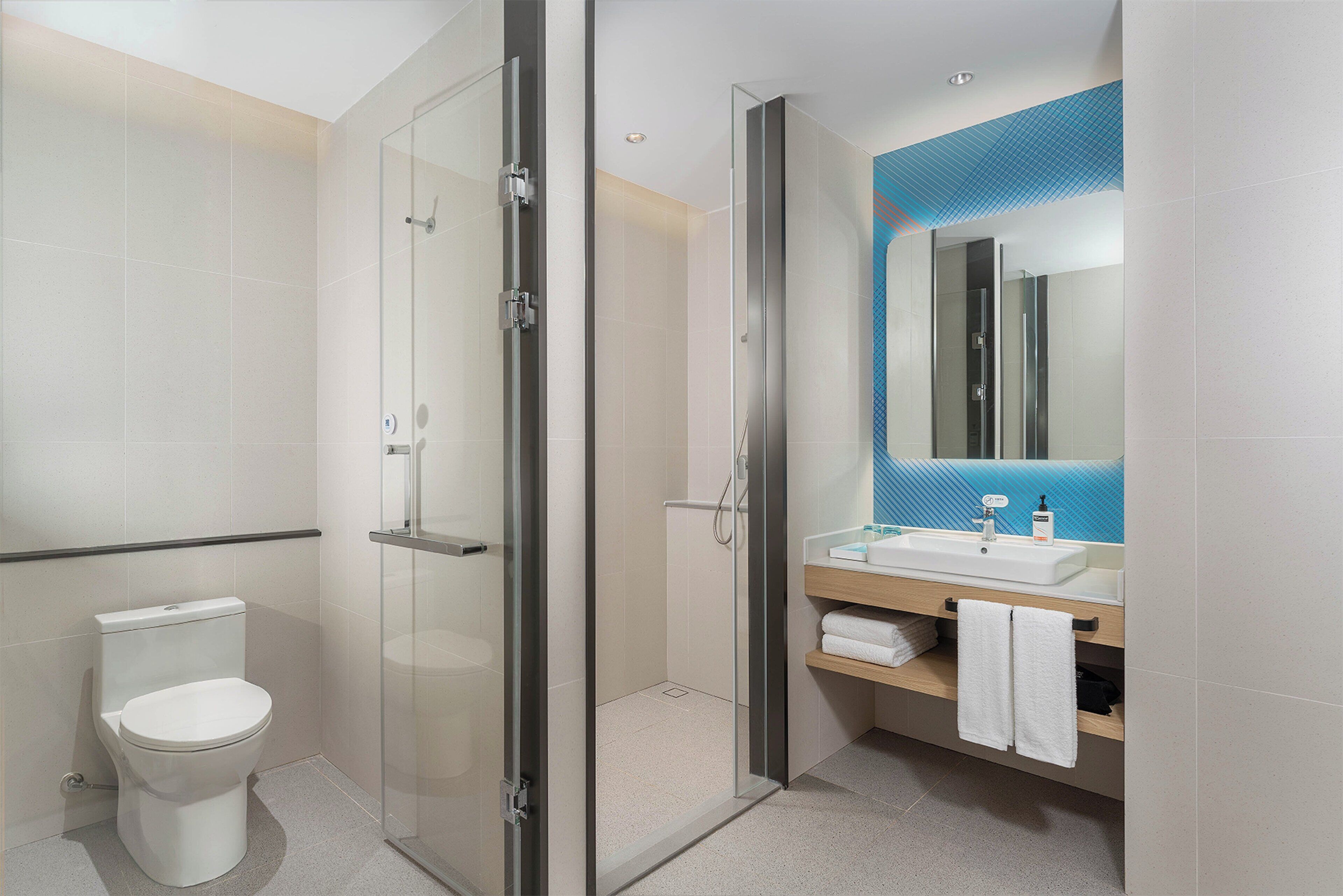 Un baño moderno con ducha de vidrio, inodoro blanco y lavamanos con salpicadero de azulejos azules.