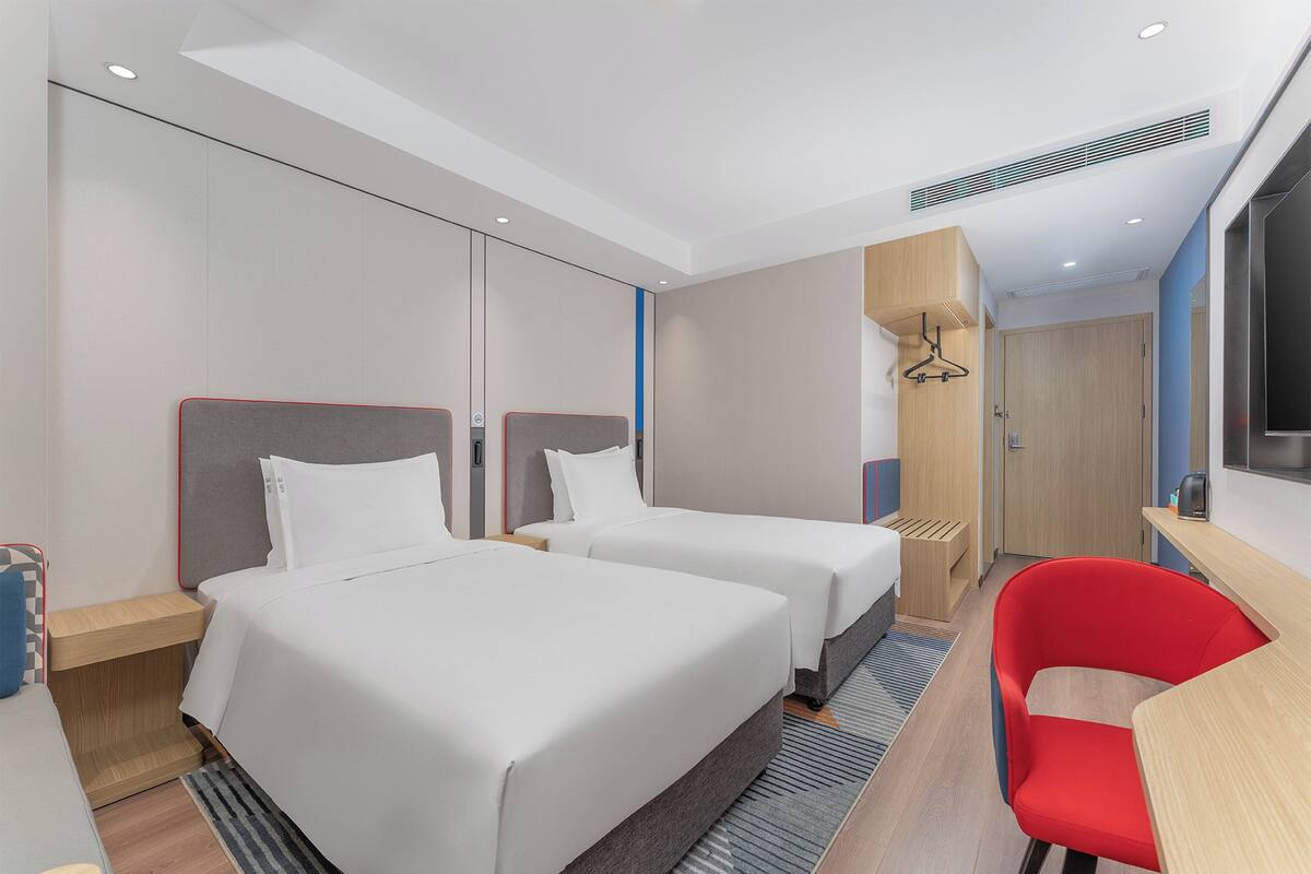 Habitación de hotel con dos camas, una silla roja, un escritorio y un armario.