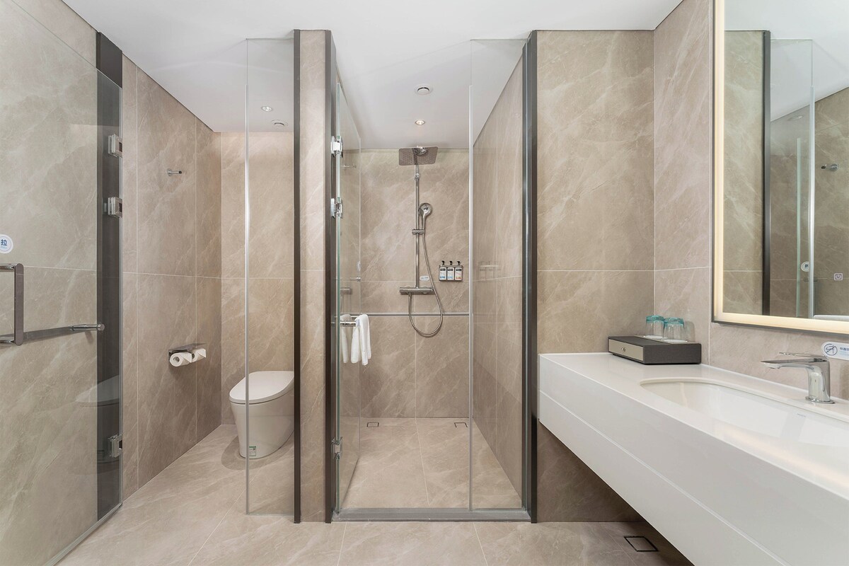 A modern bathroom with a glass-enclosed shower, a toilet, and a sink with a mirror.