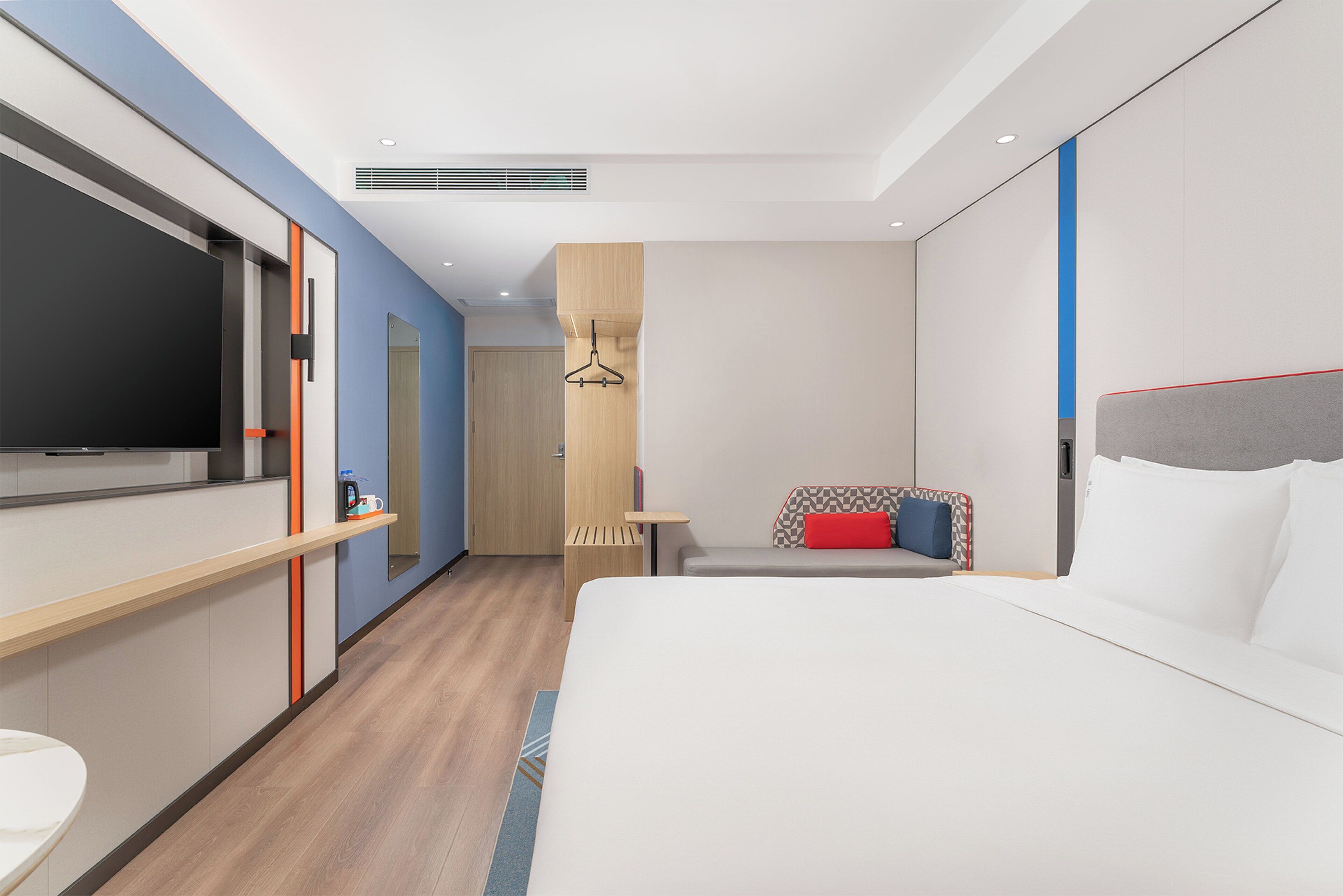 A modern hotel room with a large bed, a TV, a desk, and a bathroom.