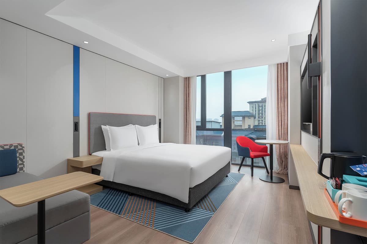 Una habitación de hotel moderna con una cama grande, un escritorio, una silla y un televisor.