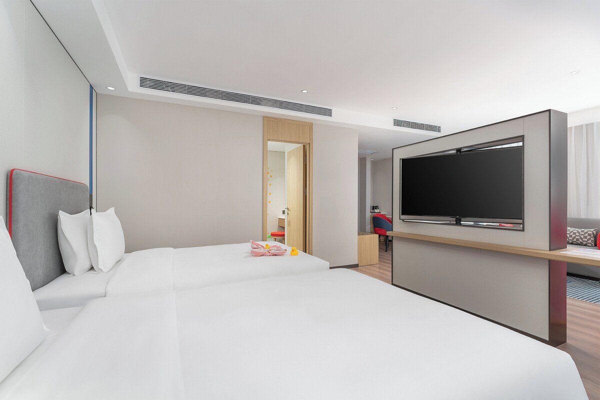 A modern hotel room with a large bed, a flat-screen TV, and a wooden desk.