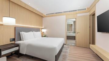Una habitación de hotel moderna con una cama grande, mesitas de noche, un televisor y un baño visible a través de una puerta abierta.